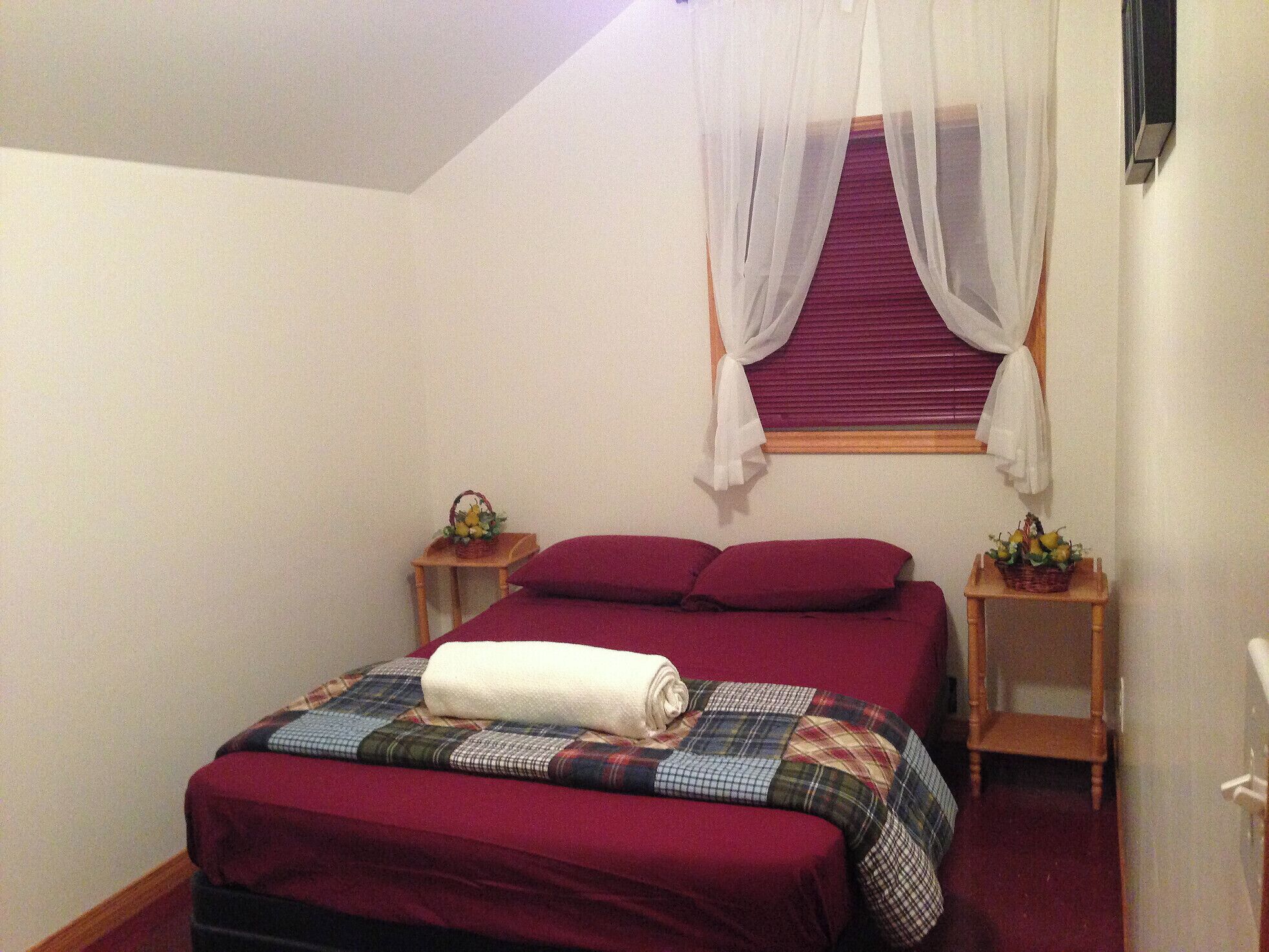 A bedroom with a bed, a window with sheer curtains, and a small table with a basket.