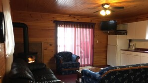 L’intérieur chaleureux d’un chalet avec une cheminée, un canapé en cuir, un fauteuil à motifs floraux et un téléviseur.