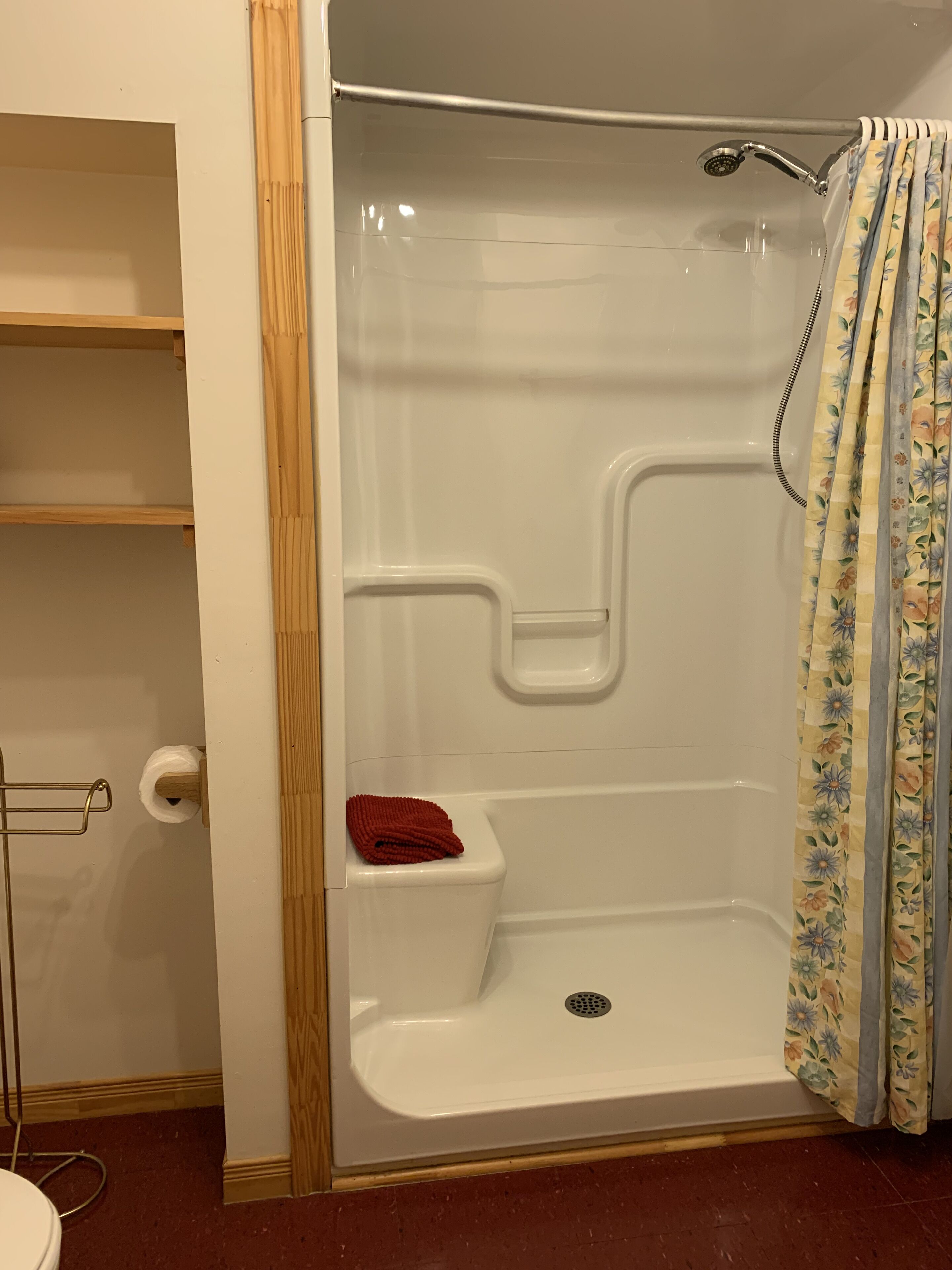 A bathroom with a shower, toilet, and a wooden shelf.