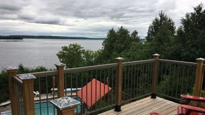 Une terrasse en bois avec une piscine, des fauteuils Adirondack rouges et une vue sur un lac.