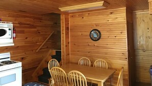 L’intérieur d’un chalet en bois comprend une table à manger, des chaises, une horloge, un four à micro-ondes et une cuisinière.