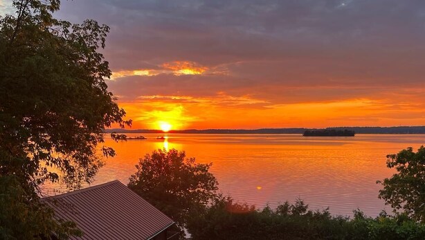 Vue d’un lac au coucher du soleil, avec une maison et un espace de détente extérieur.
