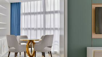 Un comedor moderno con una mesa redonda y cuatro sillas, ventanas amplias con cortinas translúcidas y una pared de acento azul.