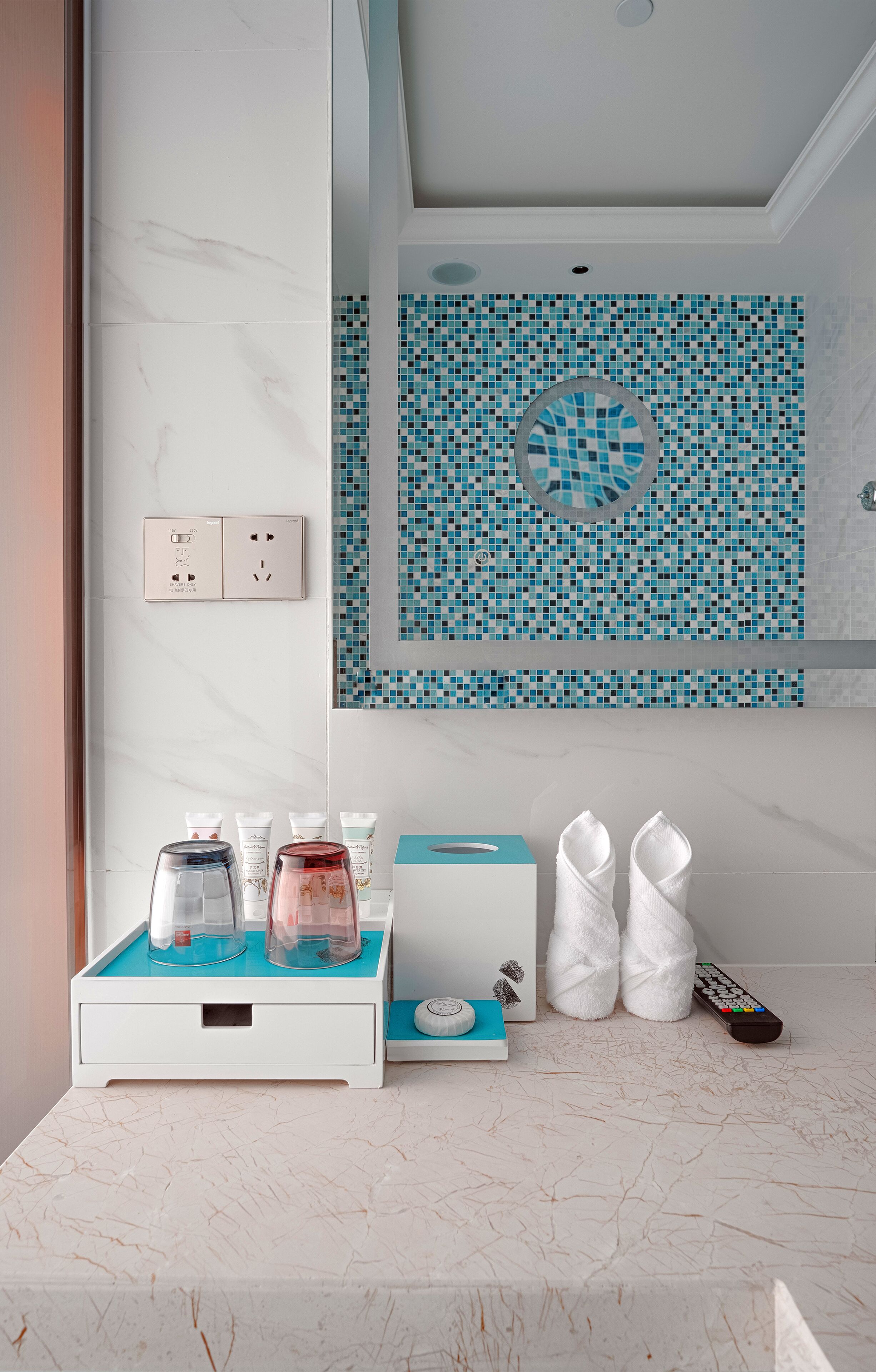Un baño con encimera de mármol blanco, pared de mosaico azul, toallero blanco y lavamanos blanco.