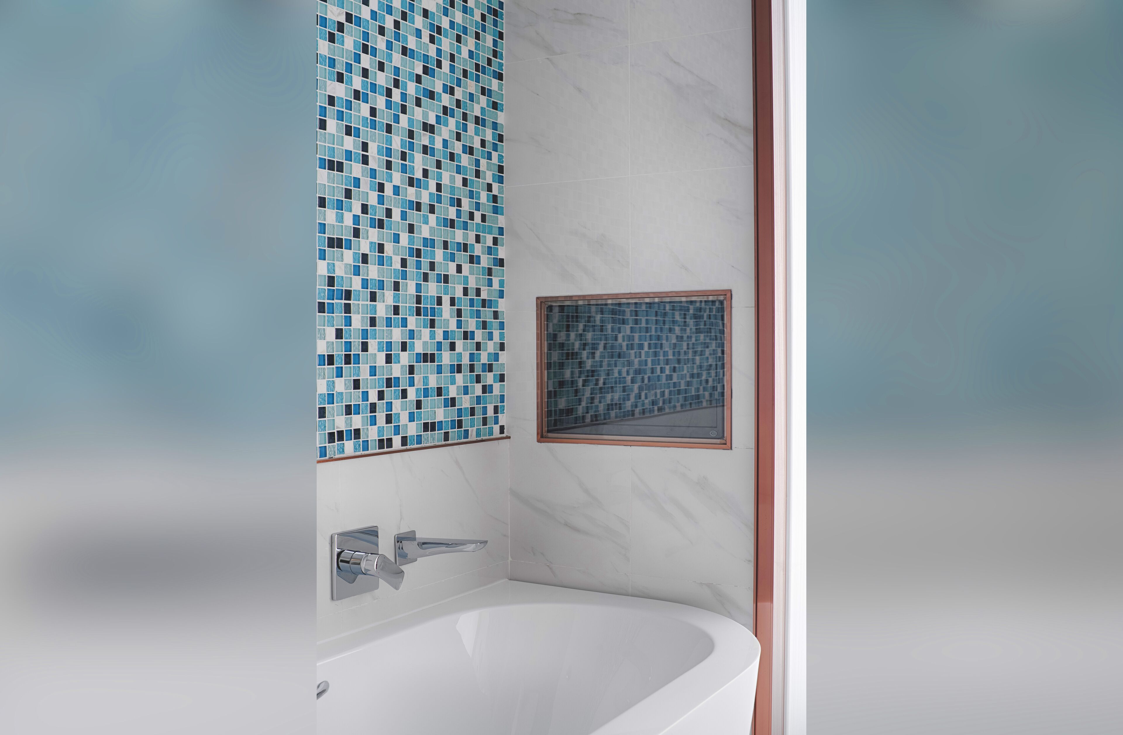 A modern bathroom with a white bathtub, a tiled wall with blue mosaic patterns, and a small framed window.