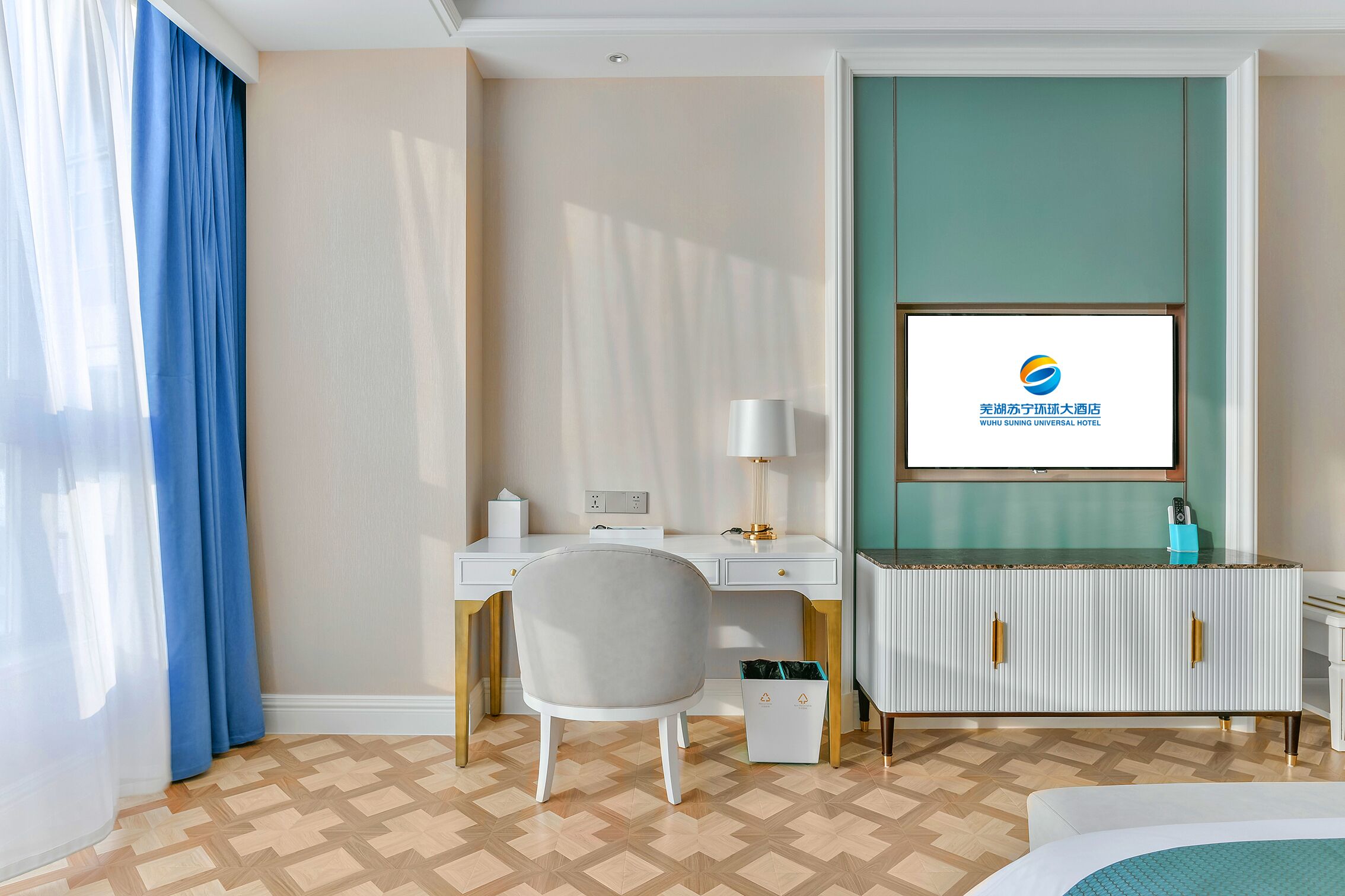 Une chambre d’hôtel équipée d’un bureau, d’une chaise et d’un téléviseur affichant le logo de l’hôtel.