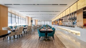 A modern restaurant with long tables and chairs, a bar area, and a large window providing natural light. - Wuhu Suning Universal Hotel (Wuhu)
