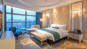A hotel room with a large bed, a smaller bed, a desk, a chair, and a view of the city through large windows. - Wuhu Suning Universal Hotel (Wuhu)