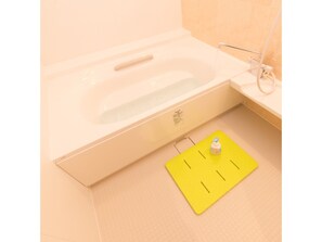 Een bad met een gele mat in een badkamer met beige tegels.