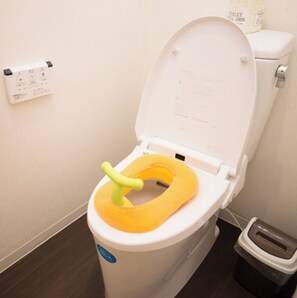 Een toilet met een gele zitting en een bedieningspaneel aan de muur.