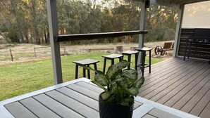 A covered patio with a table and chairs, a potted plant, and a grill area. - This Luxury Cabin is a true country retreat (Lowden)