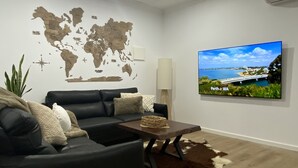 A modern living room with a black leather sofa, a wooden coffee table, a world map on the wall, and a large TV displaying Perth, WA. - This Luxury Cabin is a true country retreat (Lowden)