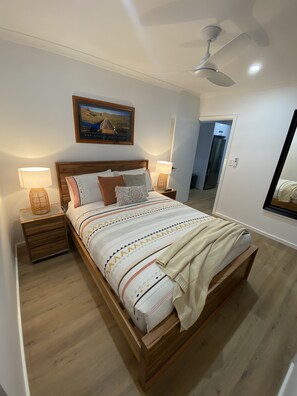 A bedroom with a wooden bed, two bedside tables with lamps, a ceiling fan, and a framed picture on the wall.