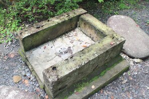 A concrete structure with a flat top and a hollow center, surrounded by gravel and greenery.