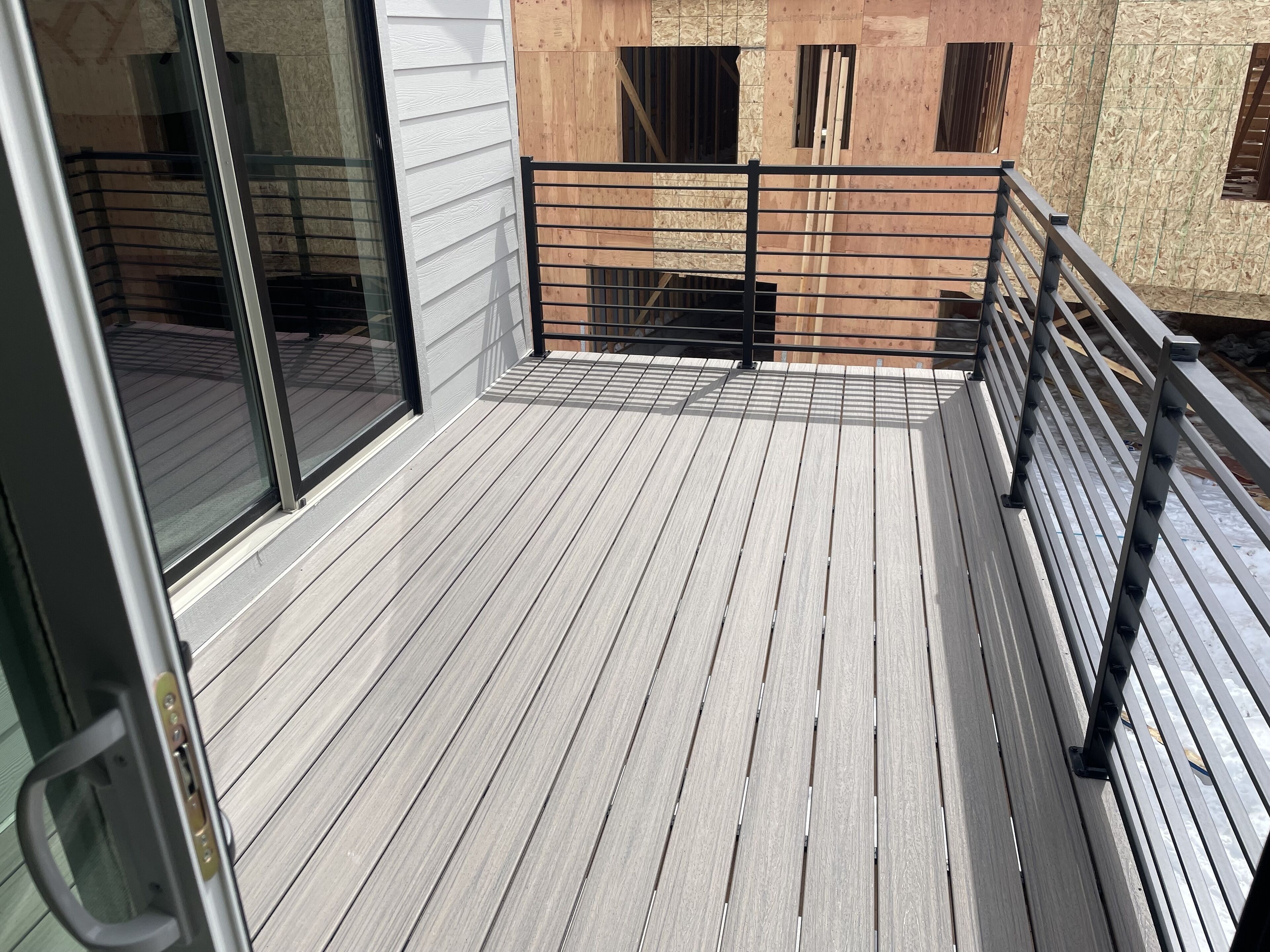 A wooden deck with a metal railing, large windows, and a view of a building under construction.