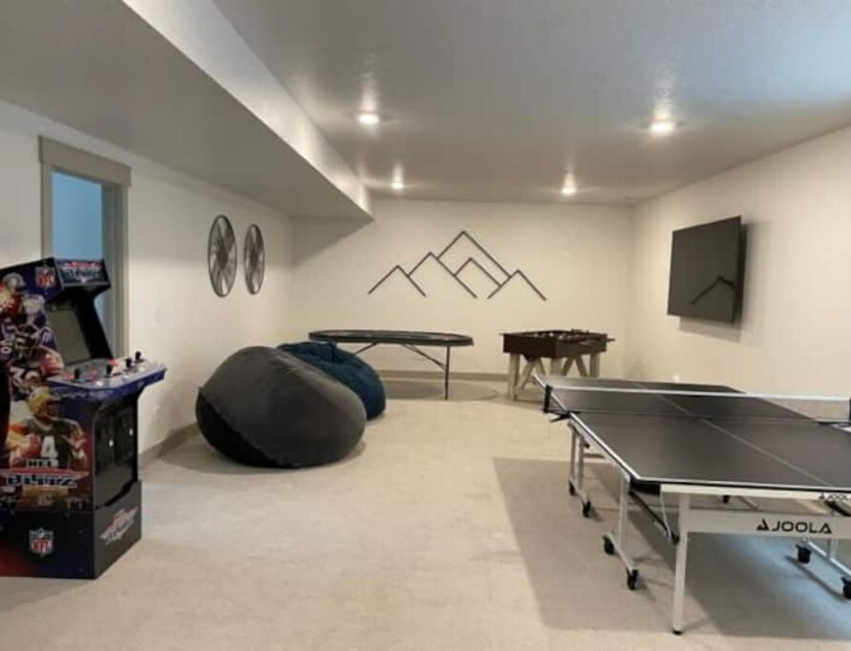 A room with a ping pong table, bean bags, a small table, and a gaming console.