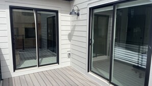A covered patio area with a wooden deck, large sliding glass doors, and a wall-mounted light fixture. - Brand New Park City Home! (Park City)