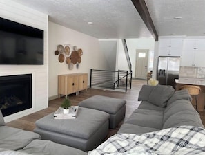 A modern living room with a fireplace, grey sofa, and a staircase leading to the kitchen.