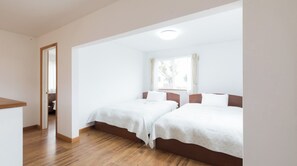Two single beds with wooden headboards and white bedding, set against a backdrop of a large window and light-colored floors.