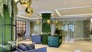 A modern lobby with a green wall, plush seating, and gold spherical lights. - Grand Eska Hotel & Suite  (Batam)