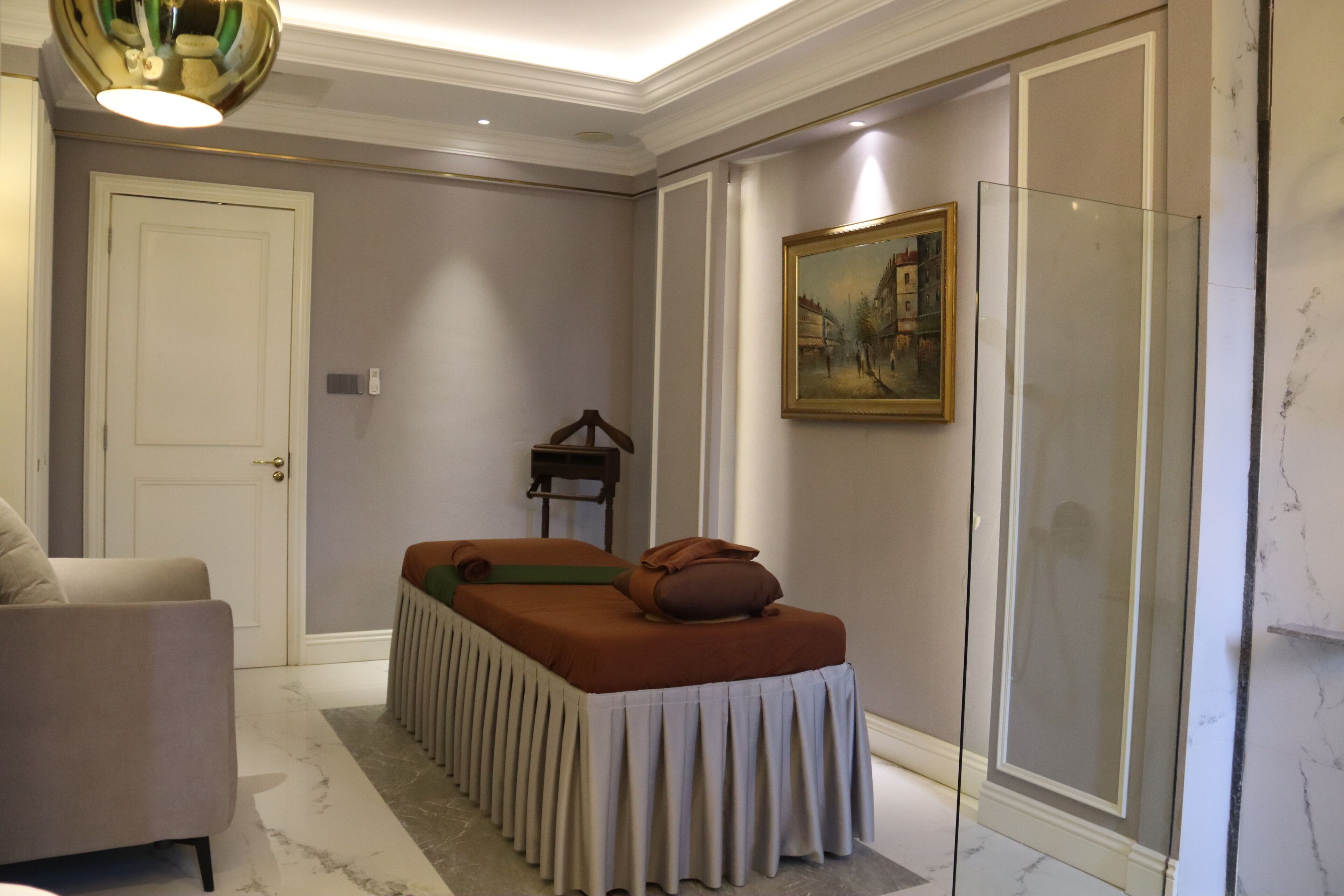 Une pièce comprenant une table de massage, un canapé, une porte, un tableau et une cloison en verre.