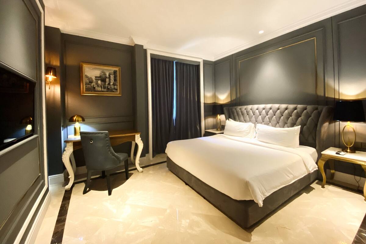 A hotel room with a large bed, a desk, a chair, and a television.
