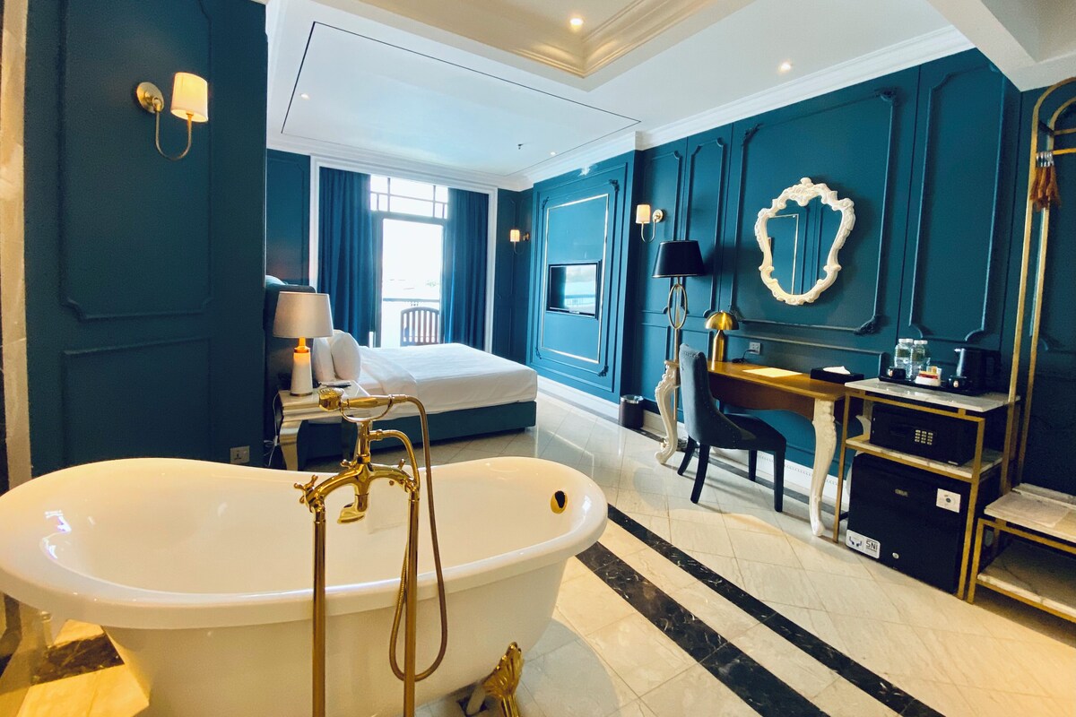 A modern bedroom with a large bathtub, a bed, a desk, and a vanity.