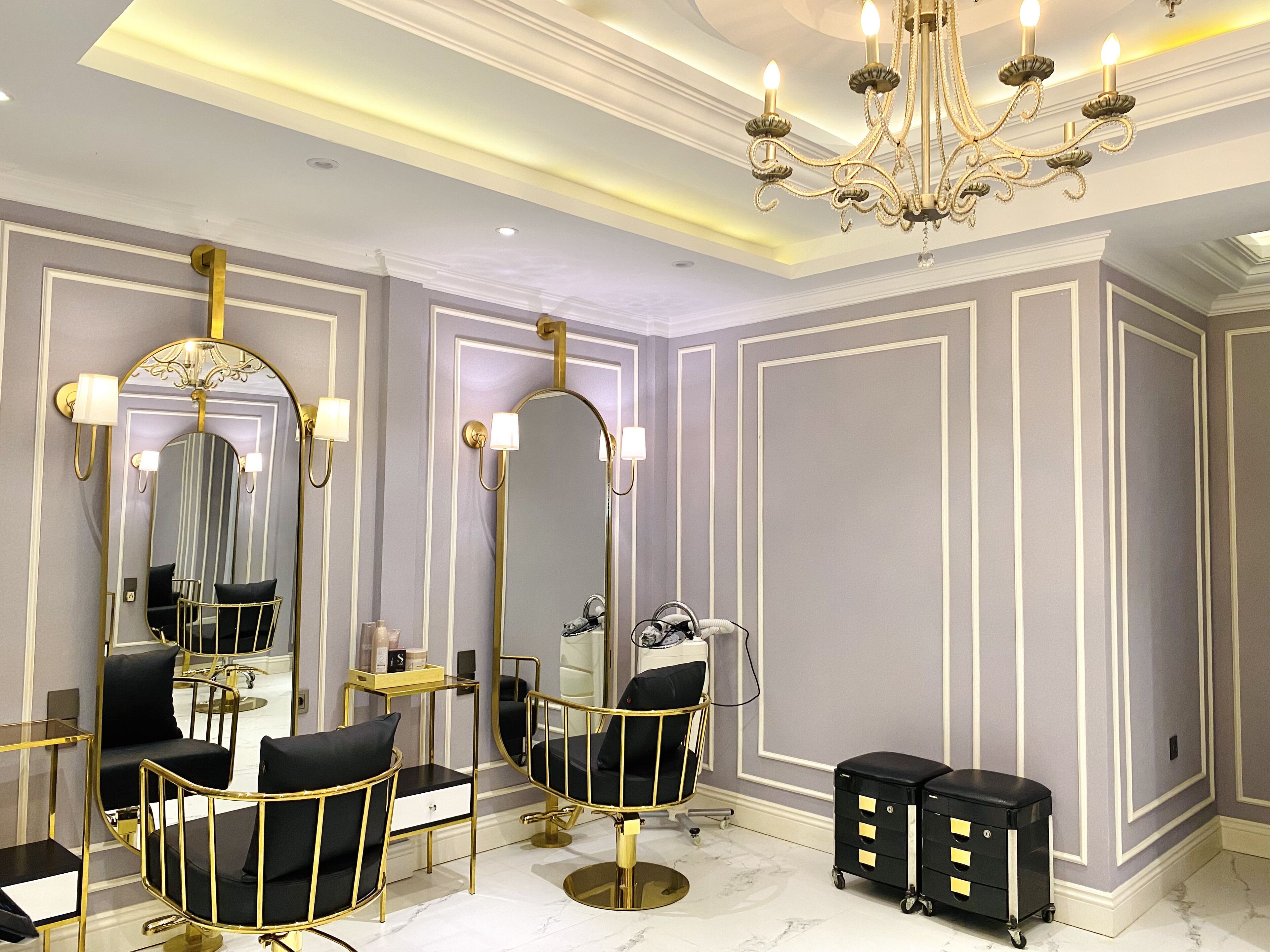 A luxurious salon with gold-framed mirrors, black salon chairs, and a chandelier.