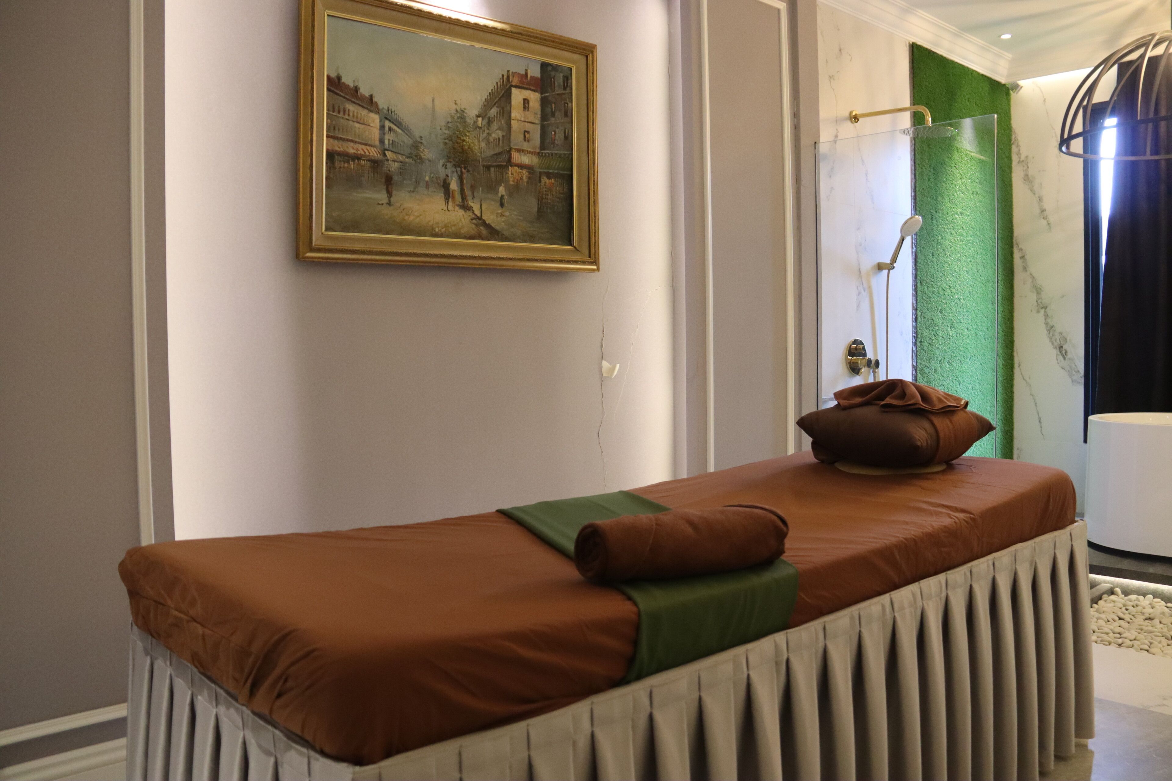 Un cuarto de spa con una camilla de masaje, un cuadro en la pared, una zona de ducha y una pared verde con textura.