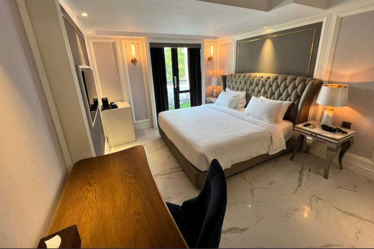 A hotel room with a large bed, a desk, a chair, a nightstand, and a lamp.