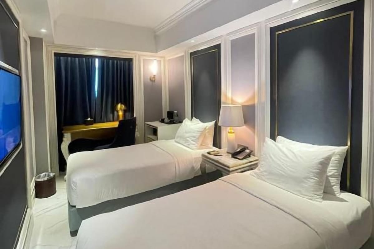 A hotel room with two beds, a TV, a desk, and a window with curtains.
