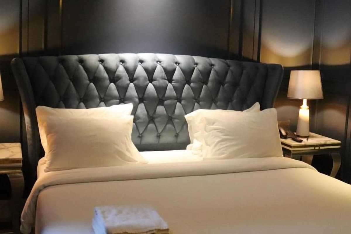 A neatly made bed with a tufted headboard, two pillows, and a folded towel on the bed.
