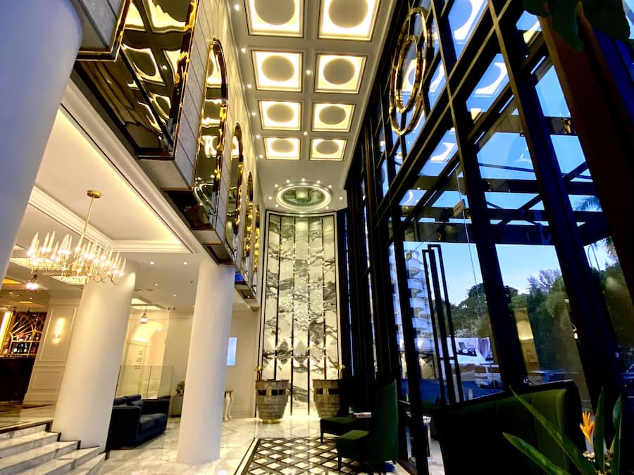 Um hall de hotel moderno com teto alto, janelas amplas e uma escadaria central.