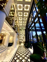 A modern hotel lobby with a high ceiling, large windows, and a central staircase.