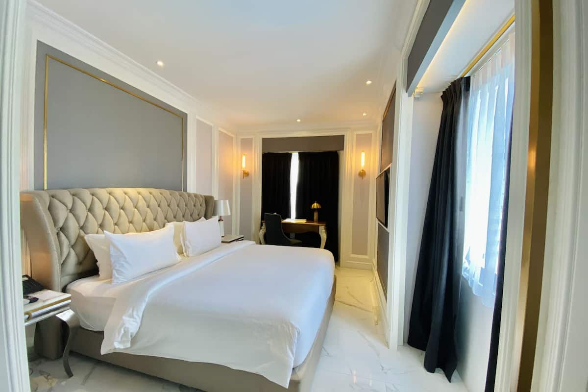 A hotel room with a large bed, a desk with a chair, a TV, and a bathroom visible through an open door.