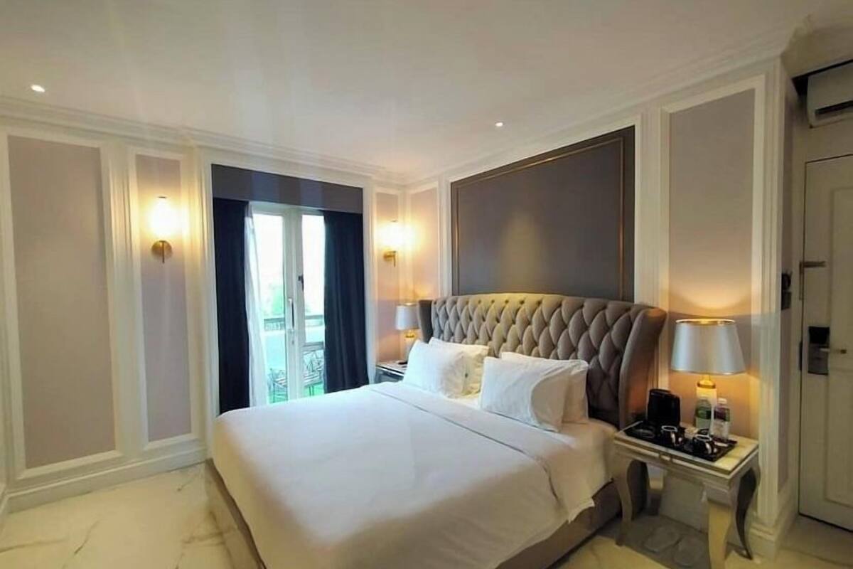 A hotel room with a large bed, two bedside tables with lamps, a view of the outdoors through a sliding door, and a door to the right.