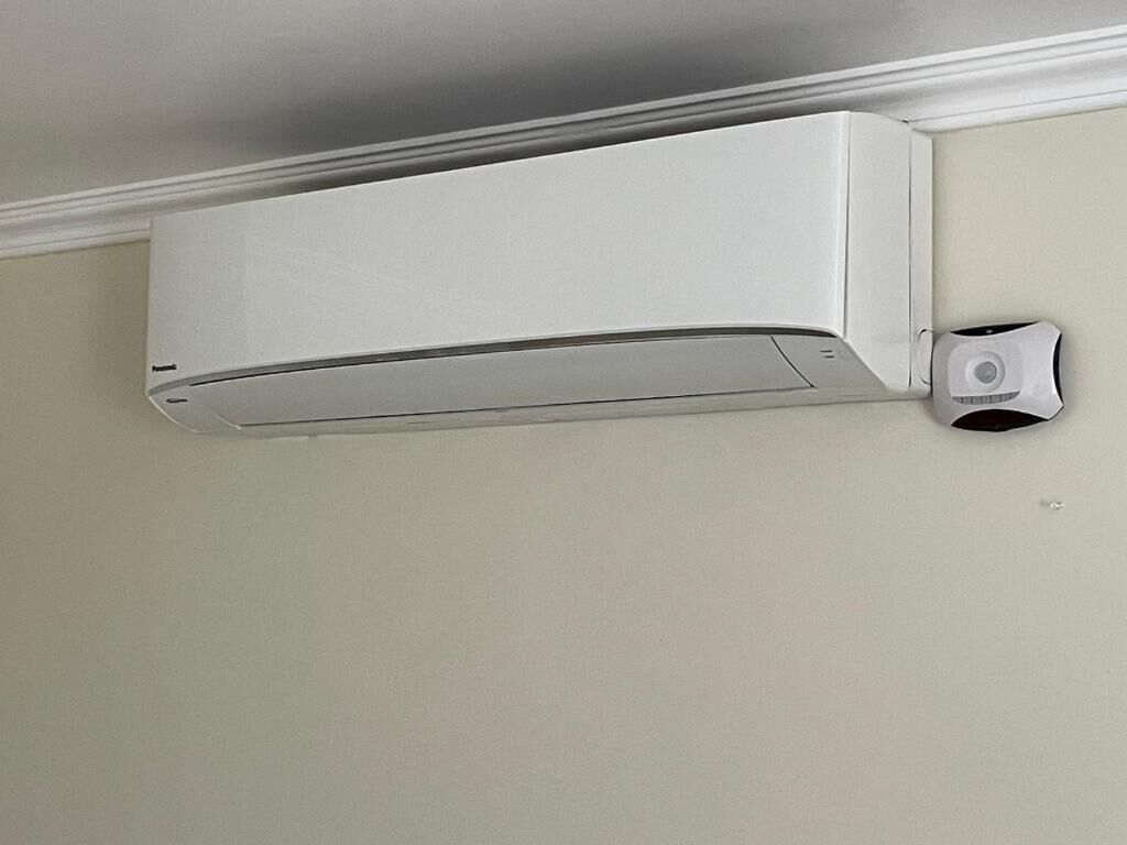 A white ceiling-mounted air conditioning unit with a control panel on the right side.