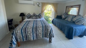 A bedroom with a bed, a desk, a chair, and a window with curtains. - Humming Bird Holiday Retreat (Ocho Rios)