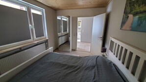 Ein Schlafzimmer mit Bett, Heizkörper, Fenster und einer Tür zu einem Badezimmer.