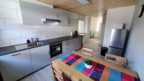 Eine moderne Küche mit grauen Schränken, einer Edelstahl-Spüle und einem eingebauten Backofen. Ein Holztisch mit farbenfroher Tischdecke und einem Topf mit Pflanze stehen bereit.