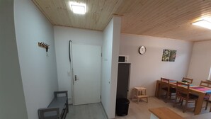 Ein gemütlicher Raum mit Holzbalkendecke, einer weißen Tür, einem kleinen Tisch mit Stühlen, einer Mikrowelle, einer Uhr und einem Mülleimer.