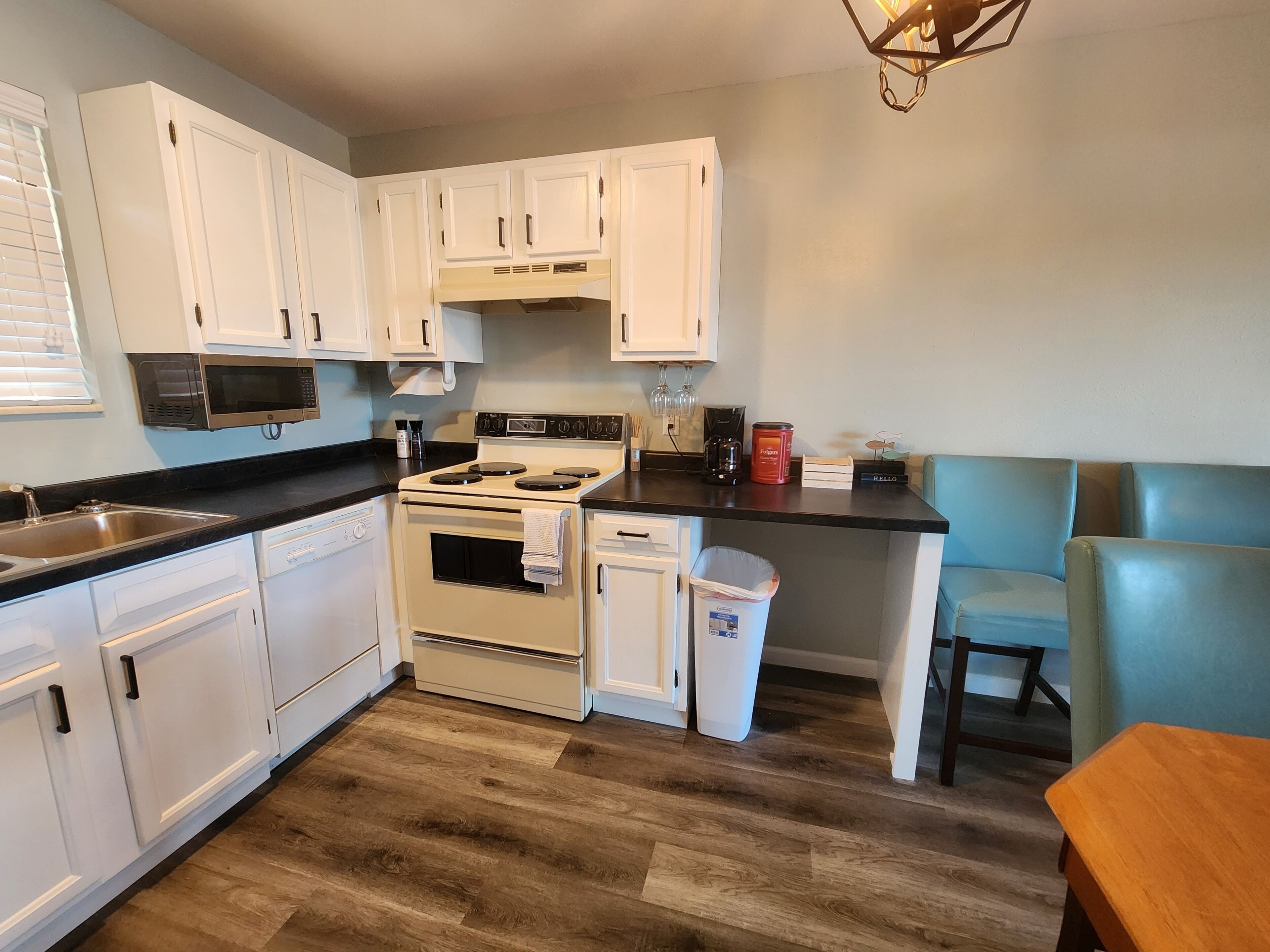 Cocina compacta con armarios blancos, estufa, microondas y cafetera.