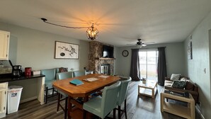 Un coin repas avec une table et des chaises en bois, une cuisine avec un mur en pierre, une cheminée et un salon avec un canapé et une table basse.
