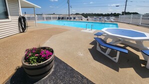 Un espace piscine avec un transat et une table, le tout entouré d’une clôture blanche.