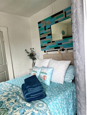 Une chambre à coucher avec un lit, des oreillers, une serviette pliée, un miroir et un élément décoratif mural.