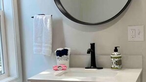 Un baño con un espejo redondo, lavamanos blanco, grifo negro y un armario debajo.