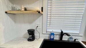 A kitchen with a sink, countertop, cabinets, a coffee maker, and a window with blinds.