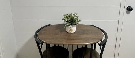 A dining area with a round wooden table, two black chairs, and a small potted plant.