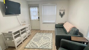 A living room with a wooden floor, a green sofa, a white entertainment unit, and a patterned rug.