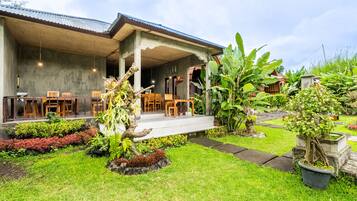 A covered outdoor seating area with tables and chairs, surrounded by lush greenery and potted plants.
